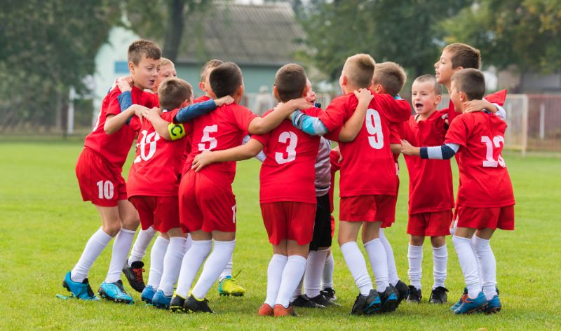 GettyImages-613520120 A group of young boys in red soccer uniforms huddle in a circle on a grass field.