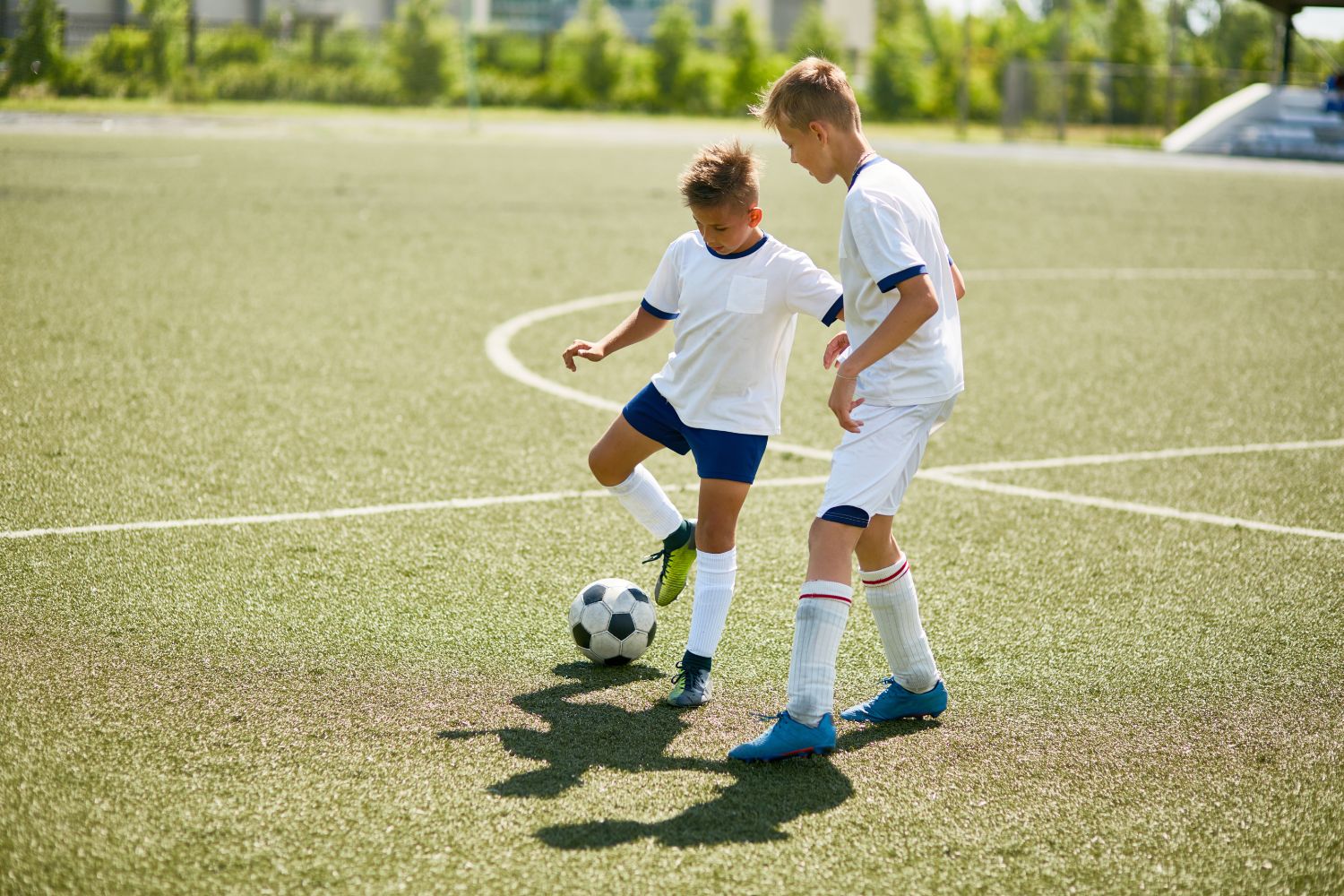 GettyImages-827507398 Two boys in white soccer uniforms play with a soccer ball on a green field.